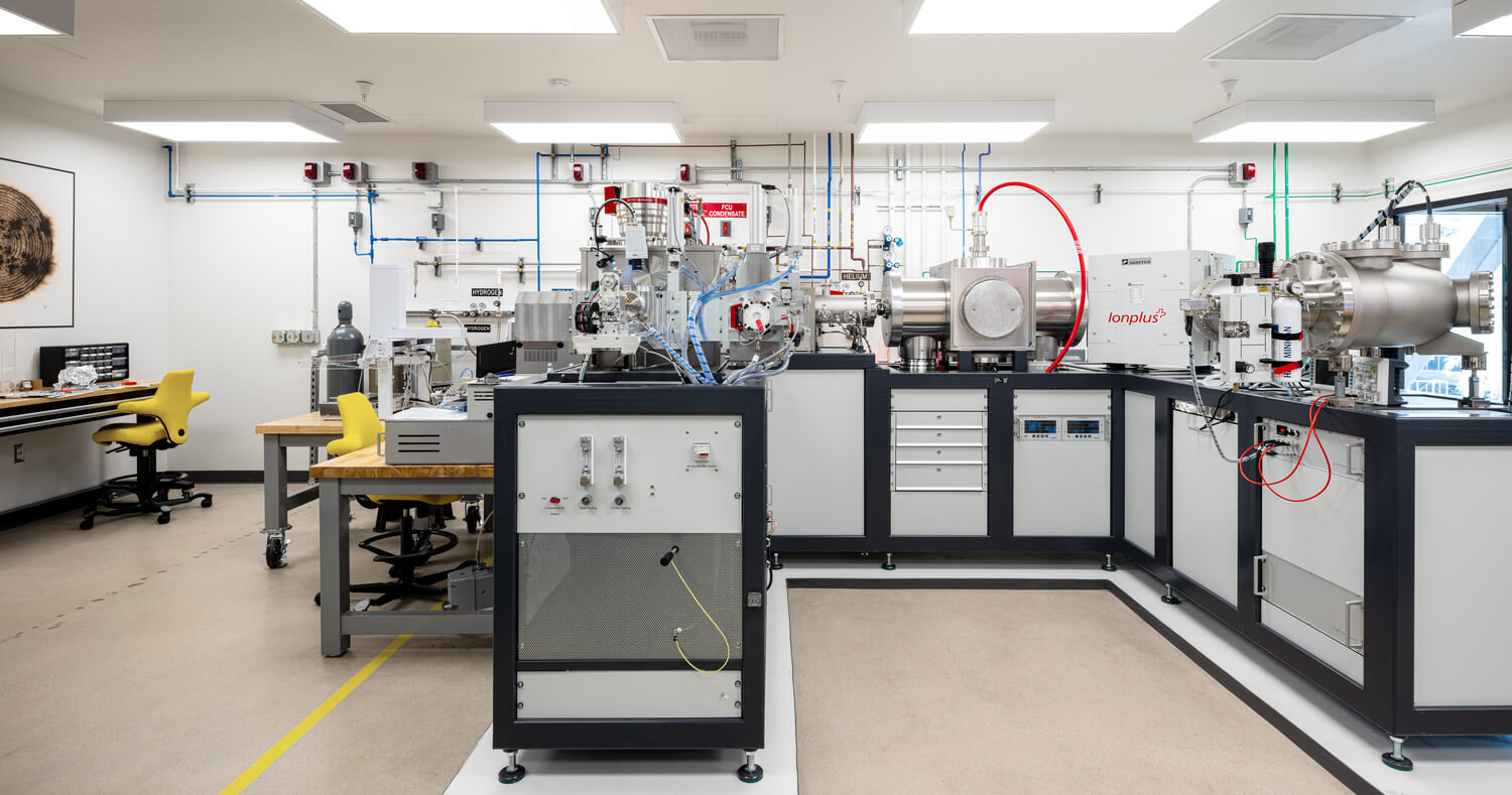 Advanced laboratory featuring high-tech mass spectrometry equipment and precision instrumentation, with bright lighting, organized workstations, and yellow lab chairs.